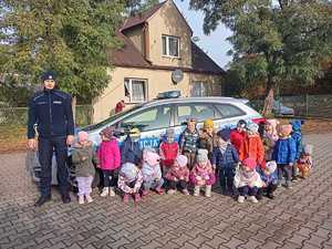 grupa dzieci z policjantem stoją przed radiowozem